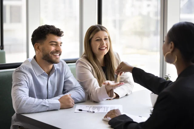 Property manager handing keys to happy tenants — benefits of hiring a property manager.